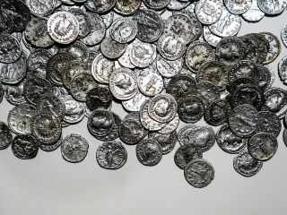 Tesoretto di monete antiche in argento su una superficie chiara. Le monete presentano rilievi con profili umani e iscrizioni lungo i bordi. Risalgono al terzo secolo d.C.