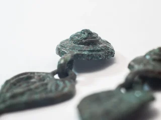 Primo piano di piccoli orecchini pendenti cuoriformi in bronzo di epoca medievale. Gli oggetti sono appoggiati su uno sfondo bianco, con alcune parti sfocate in primo piano e sullo sfondo.