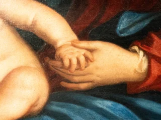Dettaglio di un dipinto a olio che ritrae a Madonna con bambino e allegoria della Giustizia del Padovanino. La mano della Vergine sorregge con dolcezza la mano piccola di Gesù bambino. Sullo sfondo si notano panneggi di vesti nei colori rosso e blu.