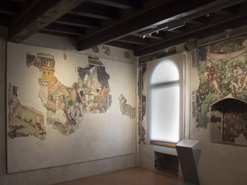 Sala storica con frammenti di affresco medievale raffiguranti scene della leggenda di Tristano e Isotta, dipinti sulle pareti laterali.
