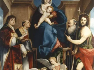 Pala d’altare di Giovanni Antonio de’ Sacchis detto il Pordenone. Dipinto di grandi dimensioni che raffigura la Madonna in trono con il Bambino Gesù in piedi sulle sue ginocchia. La Vergine indossa un abito rosso e un ampio mantello blu. Ai lati del trono sono disposti quattro santi: sulla sinistra due figure in abiti ecclesiastici riccamente decorati, uno dei quali tiene un libro; sulla destra un santo anziano con la barba bianca e San Giovanni Battista, riconoscibile dalla croce di canna e dal mantello rosso sopra la veste di pelle. Ai piedi del trono, in primo piano, due piccoli angeli musicanti siedono a terra: uno suona il liuto e l'altro un tamburello. La scena è ambientata all'interno di un'architettura classica con pilastri che lasciano intravedere un cielo azzurro sullo sfondo. La composizione è piramidale e solenne, tipica dell'arte sacra dell'epoca.