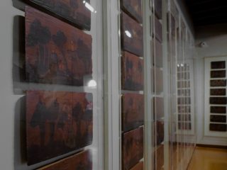 Parete di un museo con una serie di piccoli pannelli dipinti esposti dietro vetrine, disposti in sequenza lungo una sala.