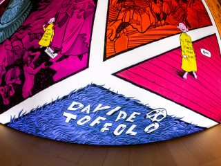 Dettaglio della tavola Quasi Fumetto di Davide Toffolo. La sezione blu in basso con texture a forma di pelo di animale riporta la firma dell'artista "DAVIDE TOFFOLO" in grandi caratteri bianchi stilizzati, accompagnata dal disegno di un piccolo teschio.