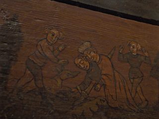Dettaglio di un pannello ligneo dipinto, con una scena figurativa stilizzata raffigurante più personaggi, visibilmente consumata dal tempo.