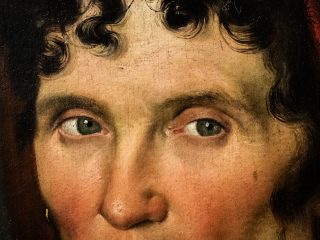 Un primo piano ravvicinato in stile fotorealistico del dipinto a olio originale, concentrandosi sulla zona del viso e degli occhi della figura femminile. L'immagine cattura lo sguardo attento degli occhi marrone-verdastri della figura, con i riflessi di luce nitidi e i dettagli minuti della superficie della pupilla. L'iride è circondata da una sottile linea rossa. Le ciglia, finemente rese, incorniciano gli occhi e le sopracciglia scure e curve si estendono sopra di essi. Una parte della chioma riccia e scura, con boccoli definiti che ricadono sulla fronte e sui lati del viso, è visibile. La consistenza della pelle, con le sue imperfezioni, la leggera variazione di tonalità tra le guance rosa e il resto del viso e i pori dilatati, è chiaramente visibile. Sulla guancia destra, è presente un piccolo neo scuro. Un orecchino dorato pende dal lobo dell'orecchio visibile a sinistra. Sullo sfondo scuro e indistinto, si intravede una sfumatura di colore rosso a destra. L'immagine cattura la precisione e l'attenzione ai dettagli dell'originale, con l'uso di pennellate sottili e la resa realistica dei tessuti e della pelle.