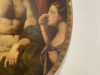 Dettaglio del Giobbe piagato di Antonio Zanchi, dipinto a olio di forma ovale racchiuso in una cornice dorata intagliata. L'opera raffigura una giovane donna di profilo che si porta una mano al naso con un'espressione sorpresa. Accanto a lei, si vede il torso muscoloso di Giobbe parzialmente coperta da un drappo verde scuro. Lo stile pittorico è classico, con un uso morbido del chiaroscuro tipico del XVII o XVIII secolo.