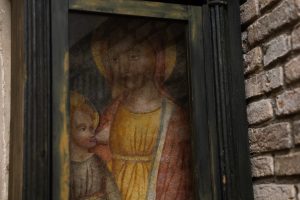 "Un dipinto antico, probabilmente un affresco, raffigurante la Madonna che allatta Ges&ugrave; bambino (iconografia della 'Madonna del Latte'). L'opera, caratterizzata da colori caldi, &egrave; protetta da una vetrata e racchiusa in una cornice di legno scuro dal gusto austero, il tutto montato su una parete rustica in mattoni a vista."