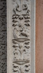 "Dettaglio di un rilievo in pietra scolpita su un pilastro verticale, suddiviso in sezioni da motivi vegetali stilizzati. Le sculture rappresentano scene allegoriche o segni zodiacali, tra cui un centauro che scaglia una freccia (Sagittario), una figura che regge una bilancia (Bilancia) e altre figure umane, il tutto arricchito da stelle incise sullo sfondo."