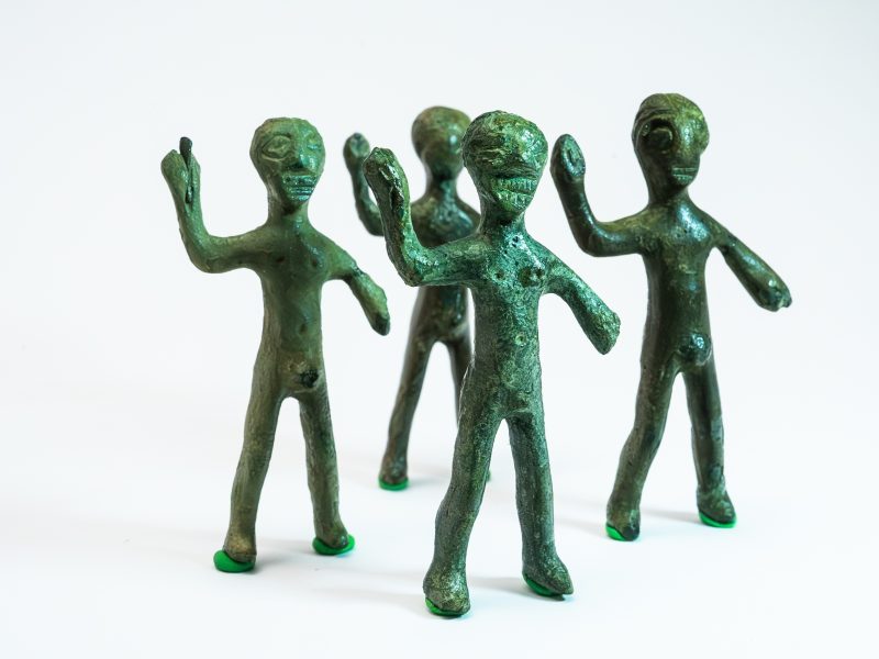 Quattro statuette antropomorfe in bronzo con patina verde sono disposte in piedi su un fondo bianco. Hanno teste stilizzate e arti allungati, con il braccio destro sollevato e piegato. Raffigurano quattro guerrieri nudi che montano la guardia. Provengono da Praturlone di Fiume Veneto e si datano agli ultimi secoli prima di Cristo.