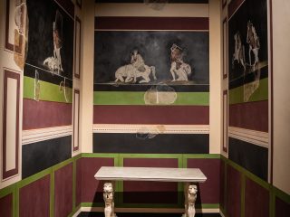 Ricostruzione museale di un ambiente romano antico della villa di Torre. Le pareti sono interamente decorate con affreschi. Al centro della parete di fondo, una scena figurativa che rappresenta un'Amazzonomachia su fondo scuro. Nella stanza è presente la ricostruzione di un tavolo in marmo bianco con gambe scolpite a forma di leoni.